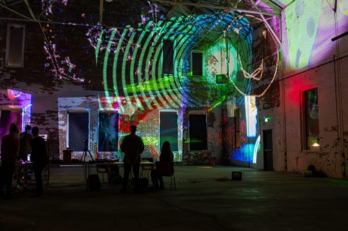 Concentric rings of green and red light projected across the brick walls of a warehouse at an OPTICKS Open Lab, Hamilton